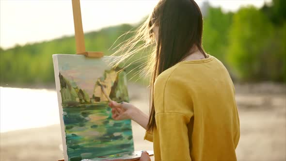 A Young Woman Paints a Painting on Canvas Which Stands on an Easel alt