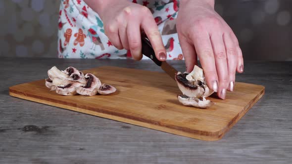A woman in a kitchen cutting up a mushroom on a wooden chopping board alt