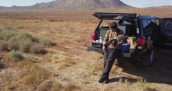 Young Man Falconer Rests on Truck Tailgate with His Falcon Hawk Raptor alt