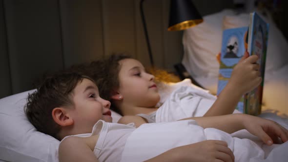 Child Care at Home Little Sister Takes Care of Younger Brother Reads a Bedtime Story to Children alt