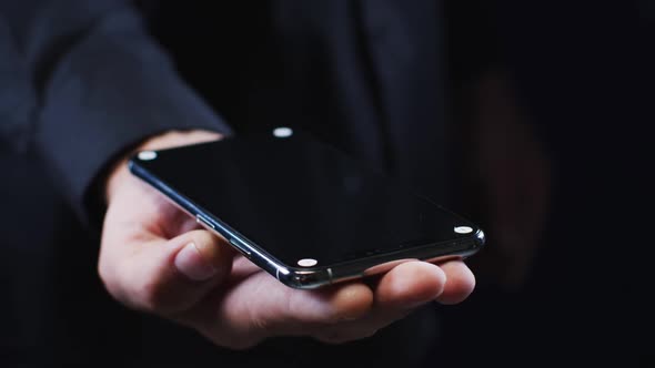 Hand of a caucasian man wearing a black shirt cradling a smartphone alt