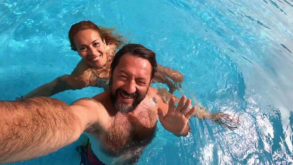 Happy caucasian people couple have fun and enjoy the swimming activity at the pool alt