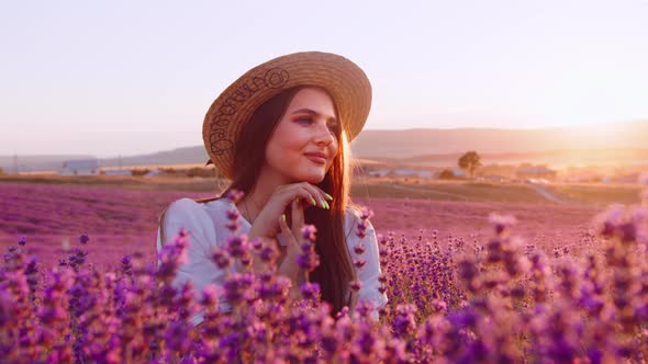 Beautiful Young Girl in a Straw Hat and White Dress Sitting in a Lavender Field on Sunset