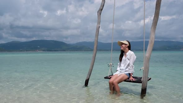 Slow motion of a beautiful young asian woman sitting on swing by the sea