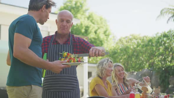Happy caucasian family having barbecue and eating in garden alt