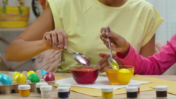 Mom and Daughter with Funny Bunny Ears Dips Eggs in Food Coloring Using Yellow and Red Paint alt