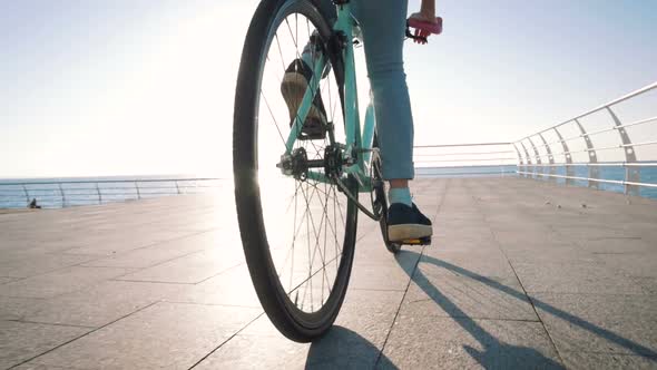Young Stylish Woman Cyclist Enjoying Fixed Gear Bike Riding Outdoors at Sunrise Near the Sea Close alt
