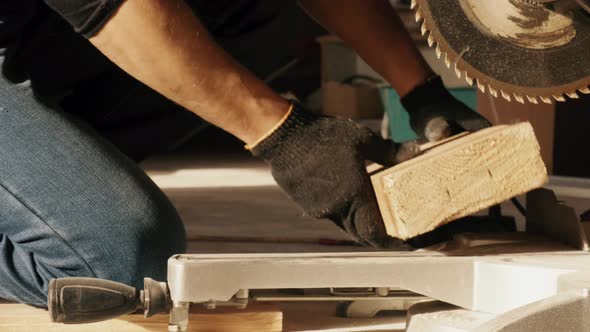 A Construction Worker on His Knees Cuts a Thick Board with an Electronic Saw