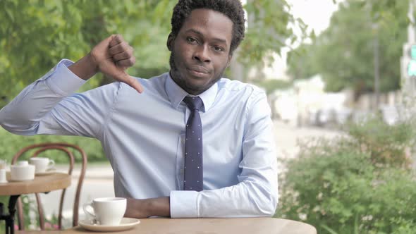 Thumbs Down by African Businessman Sitting in Outdoor Cafe alt