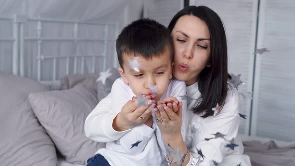 Young Mother in White Casual Clothes Plays and Hugs Her Son in the Bedroom Happiness with Confetti