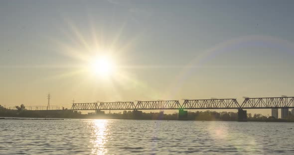 Timelapse of City River Bank. Sun Rays, Blue Sky and Railway Bridge Over Horizont. Summer Sunset alt
