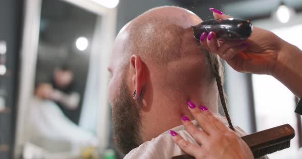 Closeup Hands of Female Barber Who Shaves the Hair of a Bearded Man Who is Sitting on the Barber's alt