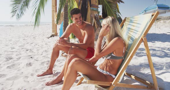 Caucasian couple sitting on sunbeds on the beach alt