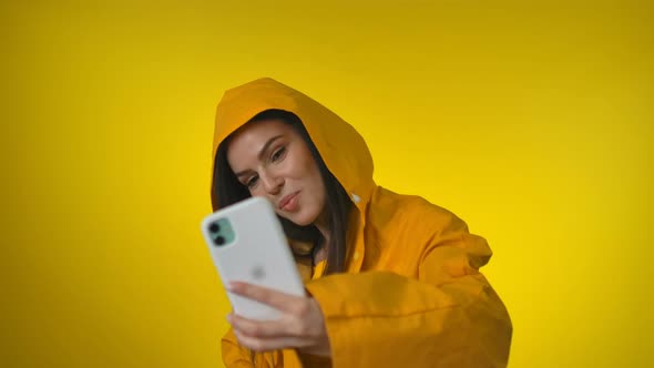 Beautiful Woman in a Bright Yellow Raincoat Makes a Selfie in the Studio alt