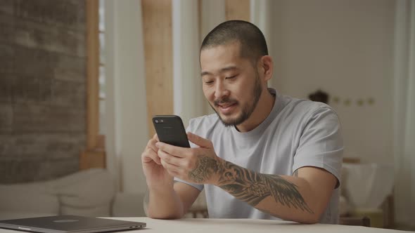 A Tattoed 20s Asian Man with Like and Dislike Facial Expressions While Browsing on Smart Phone alt