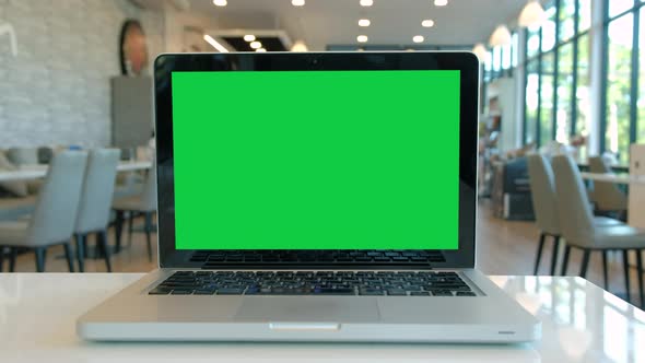 Chroma key green screen laptop computer set up for work on a cafe desk.