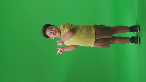 Asian Little Boy Smile And Pointing To The Side While Standing In The Green Screen Studio alt