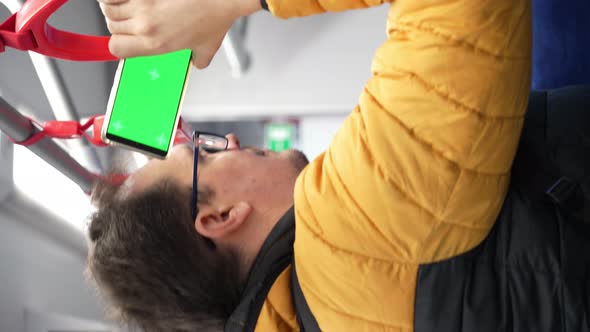 Blank Digital Phone with Chroma Key Green Screen in Hand of Guy Standing Indoors in Public Transport