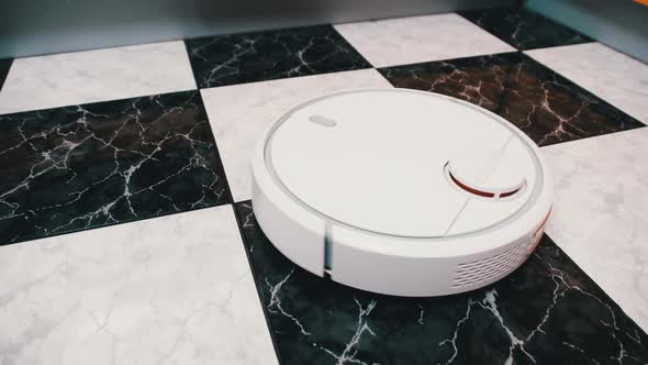 The Robot Vacuum Cleaner Cleans in the Modern House on the Tiles Floor at Kitchen alt