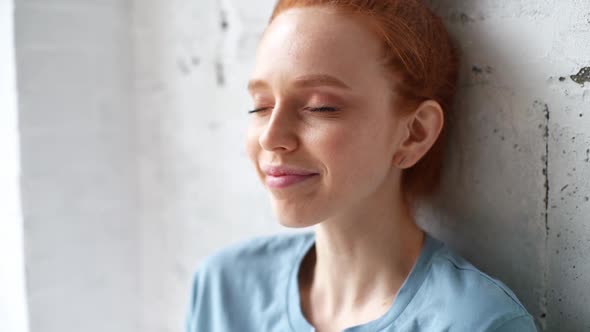 Close-up of Face of Happy Redhead Young Woman with Emotion of Joy and Success Sitting Near Window alt