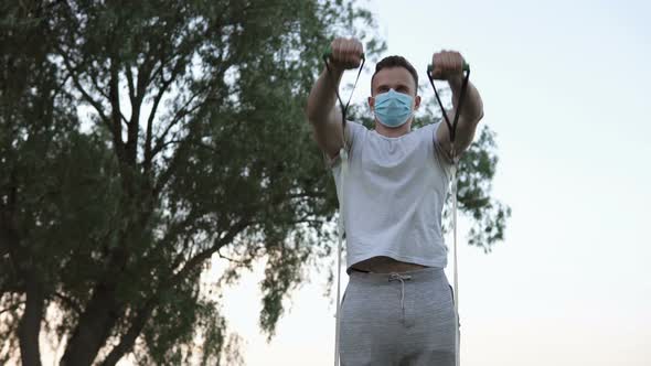 The athlete performs exercises with the help of an expander on the street in quarantine. alt