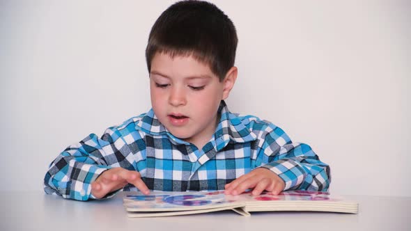 A 4Yearold Boy Looks at a Book with Thick Cardboard Pages with Pictures alt