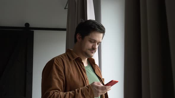 Man using mobile next to window at home