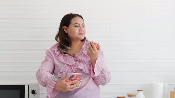 Overweight young woman eating a fresh apple, organic nutrition, vitamin C, diet in the kitchen
