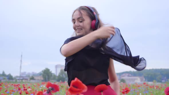 Portrait of Pretty Young Woman Wearing Headphones Listening To Music and Dancing in a Poppy Field alt