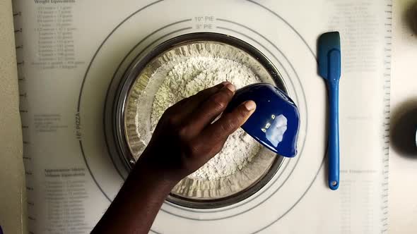 Overhead view of hands putting salt and yeast in the flour to make bread. alt