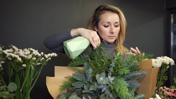 Blonde Woman Florist Splashes Water on Fir Tree Bouquet alt