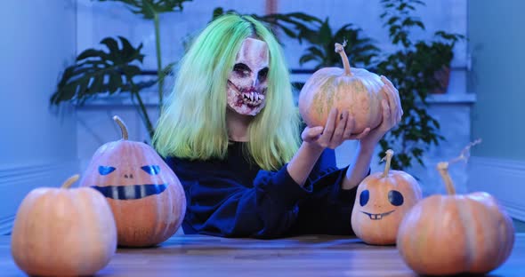 Halloween Day. Young Woman in Horrible Mask with Pumpkins
