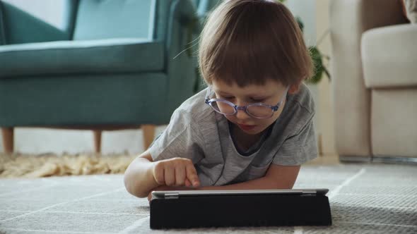 Child Using Tablet Lying on the Floor at Home Distance Learning Elearning Early Child Development alt