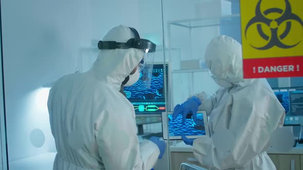 Scientists in Coverall Standing Behind the Glass Wall Working in Danger Area of Lab alt