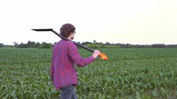 The farmer holds a shovel in his hand on an agricultural field, harvest time. alt