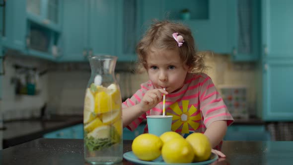 Cute preschool girl in pink t-shirt drinking glass of homemade lemonade alt