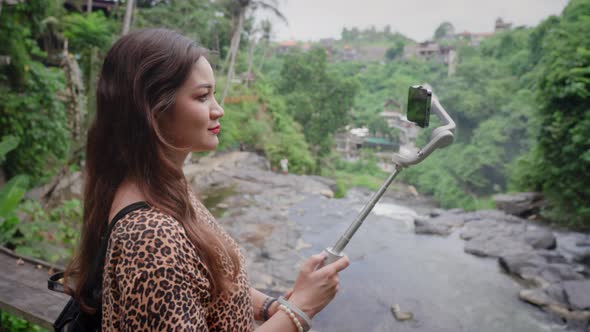 Beautiful Girl with Long Hair in Leopard Dress Holds Gray Electronic Stabilizer with Phone