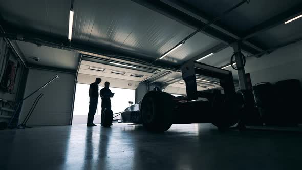 Garage with Two Men Talking While Observing a Racing Car alt