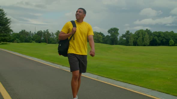 Positive Handsome African American Man with Backpack Walking in Public Park alt