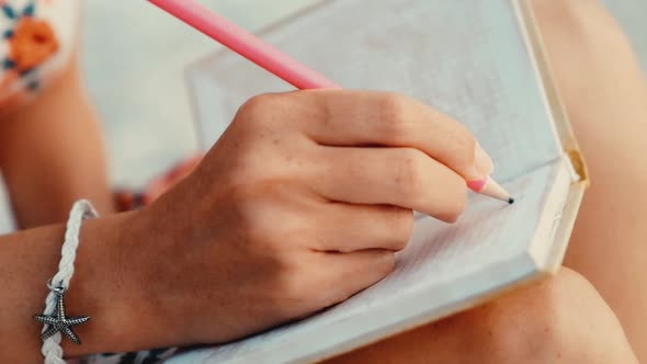 Close up view of a woman writing in her diary at sunset sitting on a beach