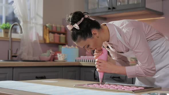Pastry Chef in Apron Piping Out Dough Mixture for Pink Macarons Shells on Slip Mat on Backing Tray alt