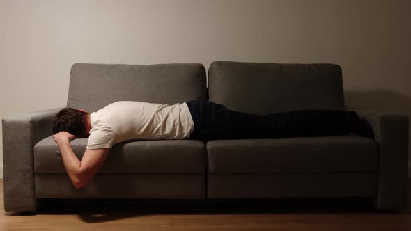 Young adult man in a white t-shirt and jeans lies on sofa in the night