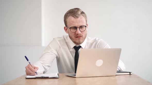 Man Accountant Has Online Business Discussion Call at Office and Writing Notes Report in Notepad