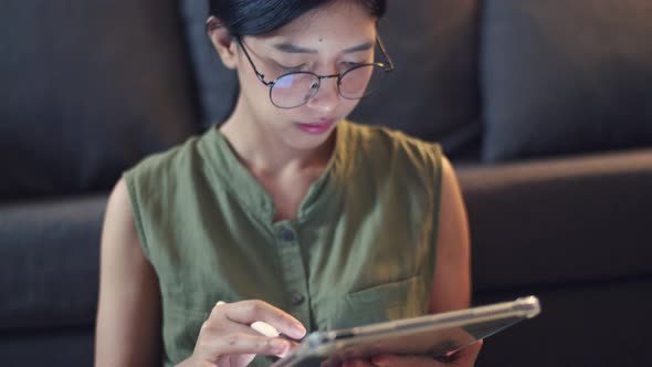 Asian female wearing glasses writes articles on her digital tablet.