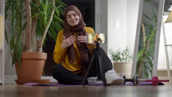 Cheerful Sport Blogger in Hijab Waving and Talking at Smartphone Streaming Online alt