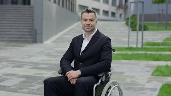 Portrait of Cheerful Man in Formal Suit Looking To Camera While Sitting at Wheel Chair alt