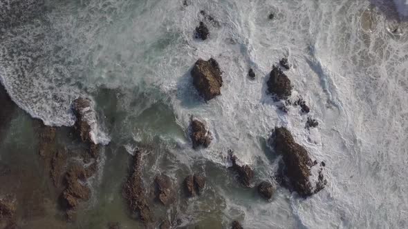 Foaming ocean waves reach rocky outcrops near shore, vertical aerial ...