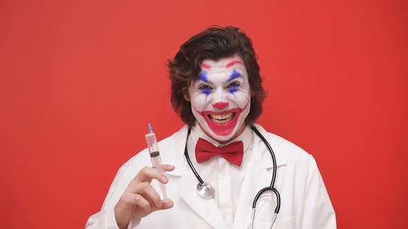 The Male Clown Doctor Prepared a Syringe Highlighted on a Red Background Intending to Treat Someone