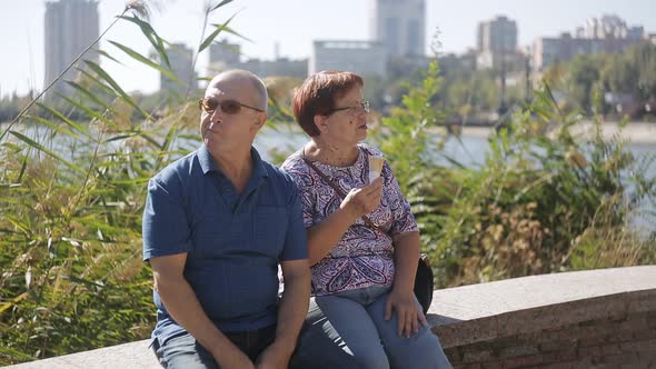 Elderly Couple Sitting on the Promenade Eating Ice Cream and Talking alt