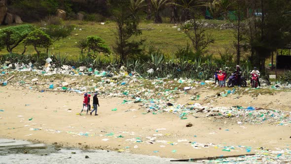 Southeast Asia villagers walking on dirty polluted beach full of plastic trash alt